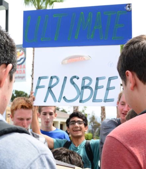 The Ultimate Frisbee club holds up a sign in order to get the attention of their peers. They even added a real frisbee to the sign, making sure everyone knew what their club was about. 
