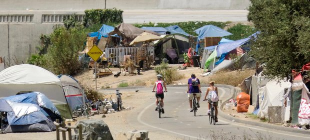 Homeless+tents+on+the+river+trail+as+visitors+bike+by.+%0A
