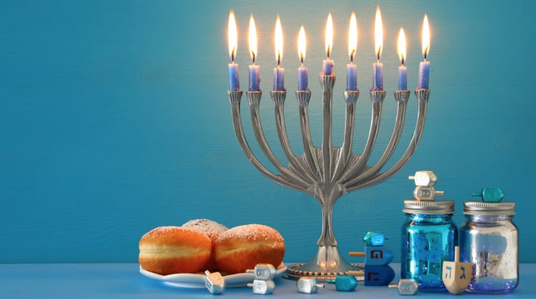 A picture of a fully lit menorah alongside sweets and dreidels for a full Hanukkah setting. 