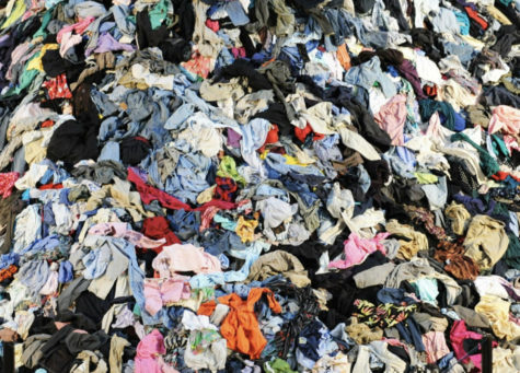 The image depicts a clothing landfill with hundreds of thousands of articles of clothing piled on top of one another. 
