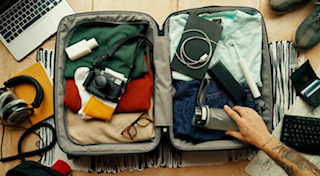 A person packing their luggage full of clothes, chargers, and other necessities. 
