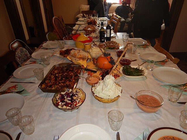 The image displays what a traditional Thanksgiving feast would commonly look like. Thanksgiving dinner table by Helena Jacoba is licensed under CC BY 2.0.